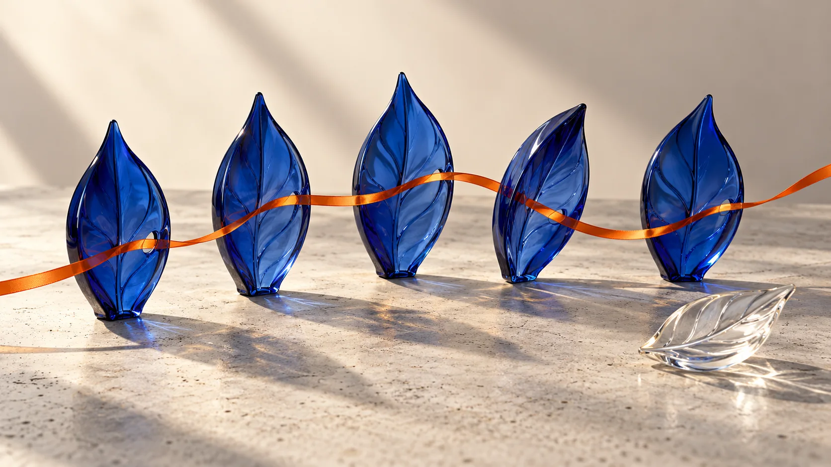 Cinco folhas de vidro azul atravessadas por fita laranja, com uma folha transparente separada sobre a mesa